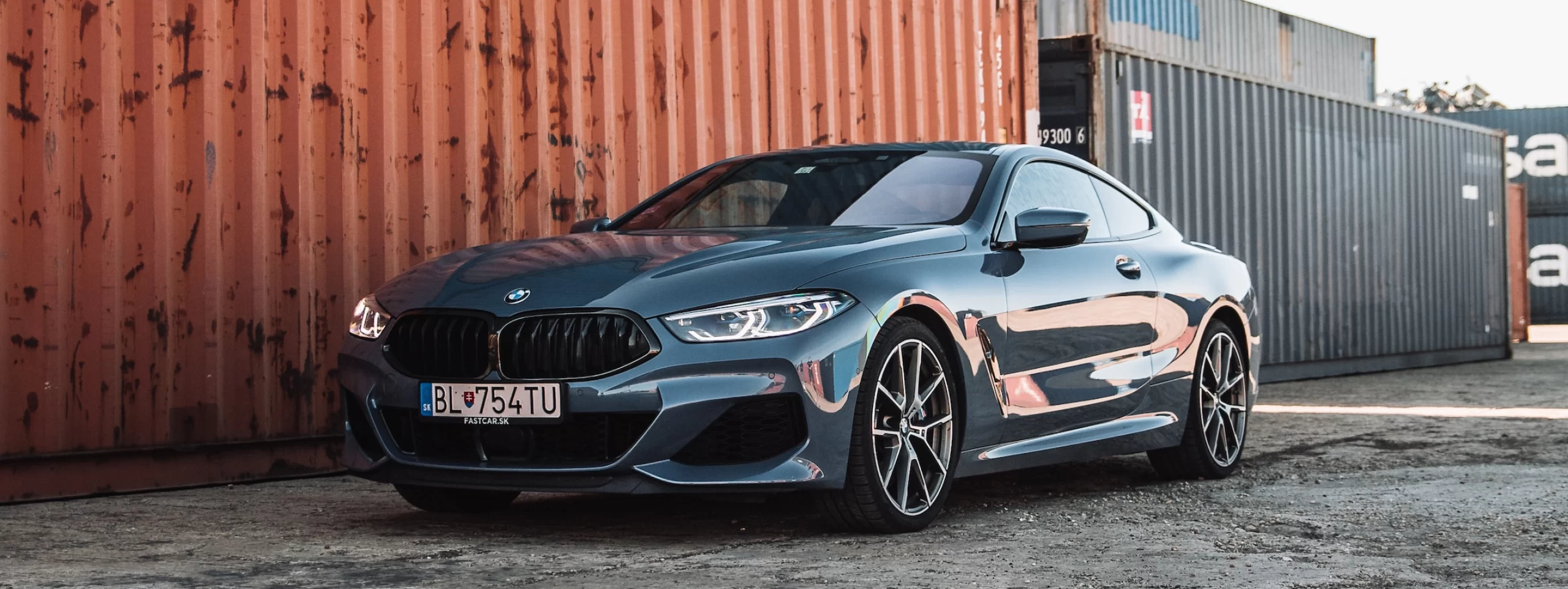 The BMW M8 Coupe is parked in front of an automotive shipping container.